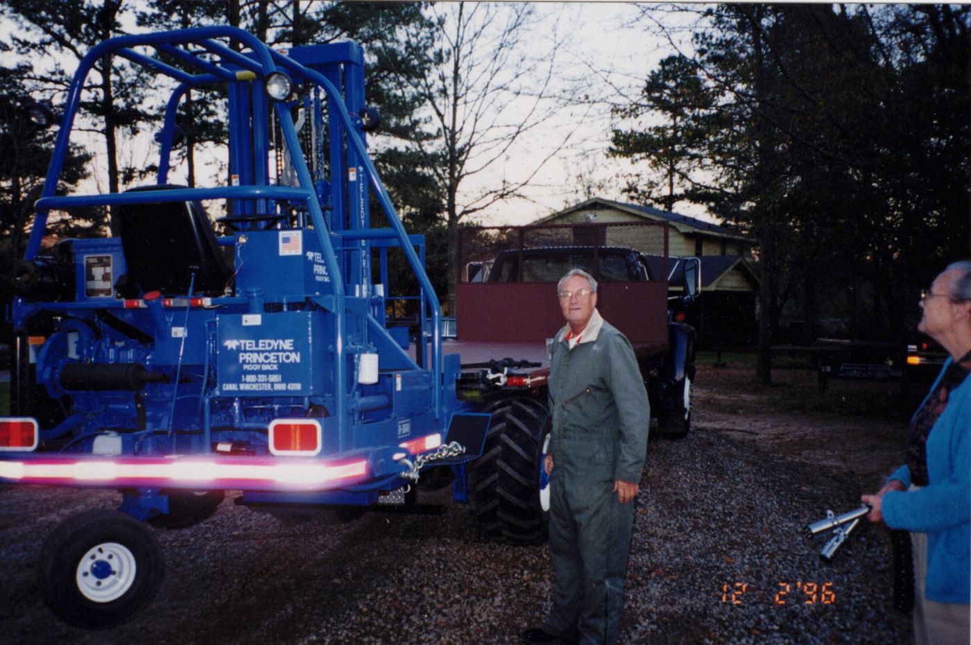 Bobby in work coveralls beside a new blue Princeton Piggyback forklift mounted on a flatbed truck