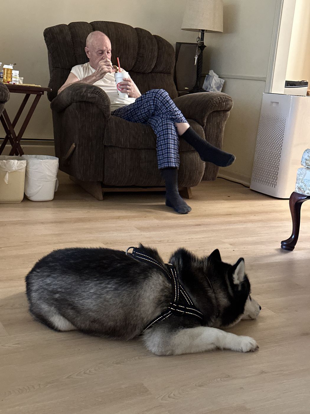 Bobby relaxing in his recliner with a cup while a great-granddog husky rests on the floor nearby